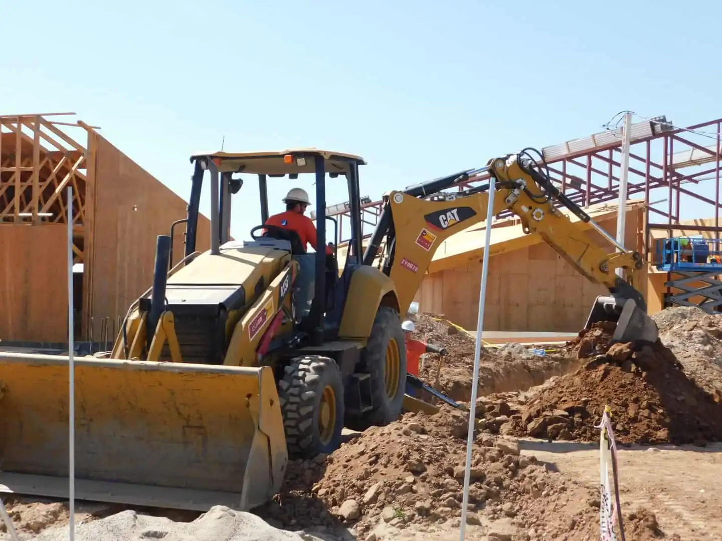 A yellow backhoe loader excavating a trench at a construction site.